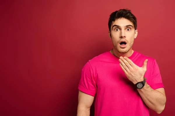 Retrato de hombre sorprendido con boca abierta en camiseta rosa sobre rojo - foto de stock