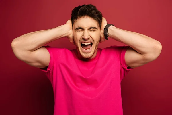 Retrato del hombre sonriente gritando y cubriendo las orejas en rojo - foto de stock