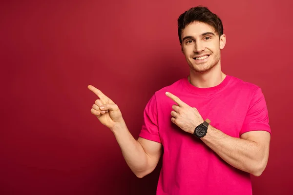 Portrait of smiling man in pink t-shirt pointing on red — Stock Photo