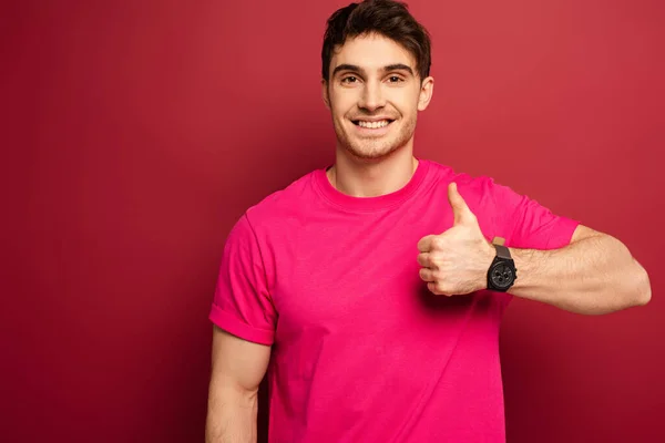 Portrait of smiling man in pink t-shirt showing thumb up on red — Stock Photo