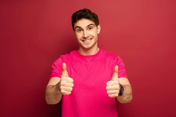 Retrato de homem feliz em rosa t-shirt mostrando polegares para cima no vermelho — Fotografia de Stock