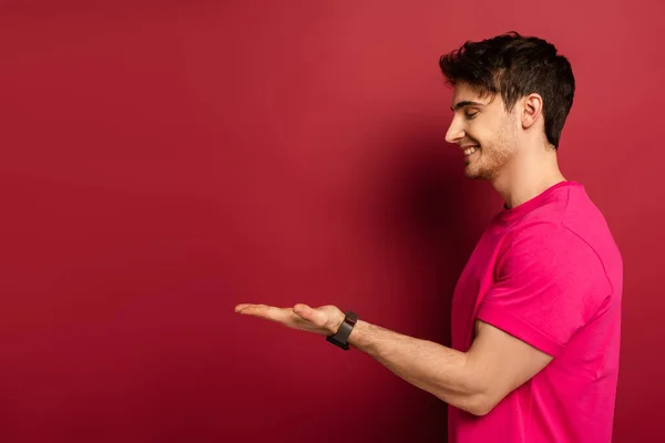 Portrait of smiling man in pink t-shirt presenting something on red — Stock Photo