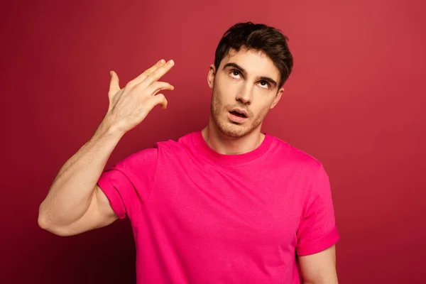 Porträt eines frustrierten Mannes im rosafarbenen T-Shirt mit Handfeuergeste auf Rot — Stockfoto