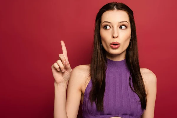 Portrait of shocked brunette woman pointing up on red — Stock Photo