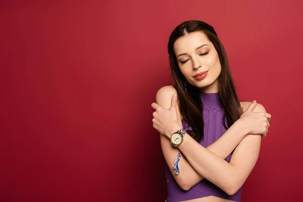 Portrait of smiling woman hugging herself on red — Stock Photo