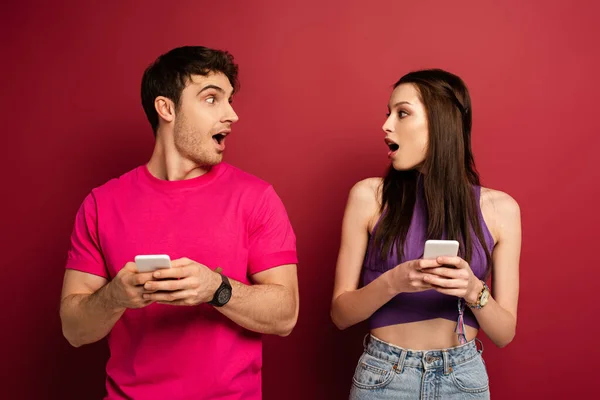 Belo casal surpreso usando smartphones no vermelho — Fotografia de Stock