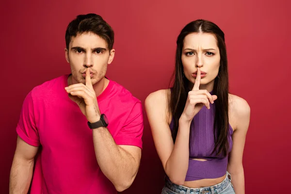 Beautiful young couple showing silence symbols on red — Stock Photo