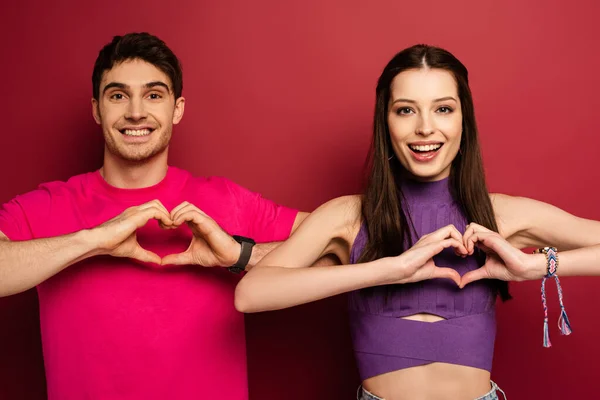 Hermosa pareja joven emocional haciendo signos del corazón con las manos en rojo - foto de stock