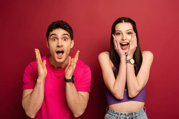 Beautiful excited young couple with open mouths on red — Stock Photo
