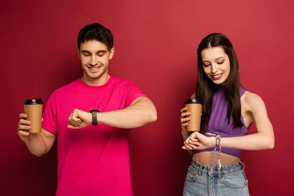 Happy couple with coffee to go looking at wristwatches on red — Stock Photo