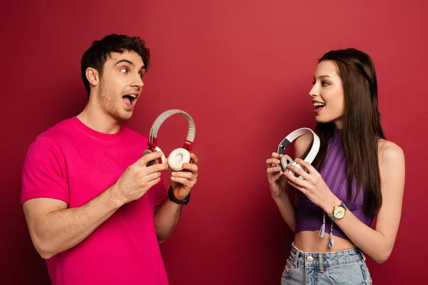 Beautiful excited couple holding headphones on red — Stock Photo