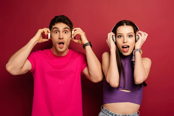 Excited couple listening music with headphones on red — Stock Photo