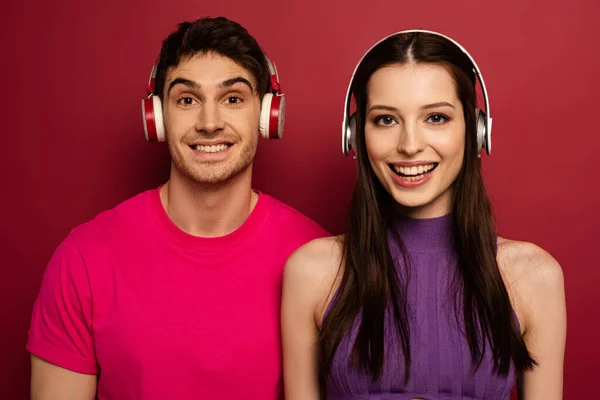 Smiling couple listening music with headphones on red — Stock Photo