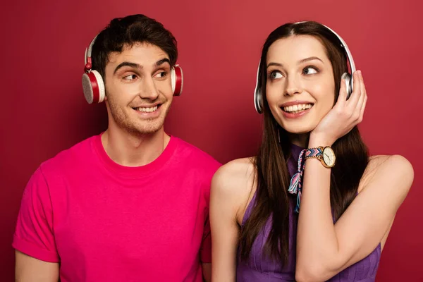 Beautiful smiling couple listening music with headphones on red — Stock Photo