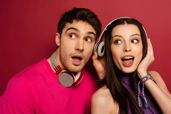 Schönes schockiertes Paar hört Musik mit Kopfhörern auf Rot — Stockfoto