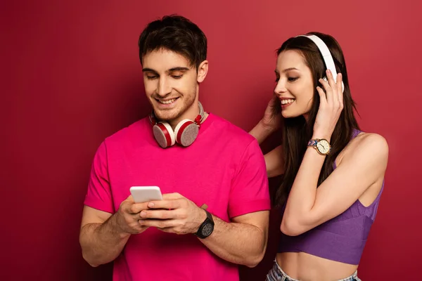 Beautiful positive couple with headphones using smartphone on red — Stock Photo