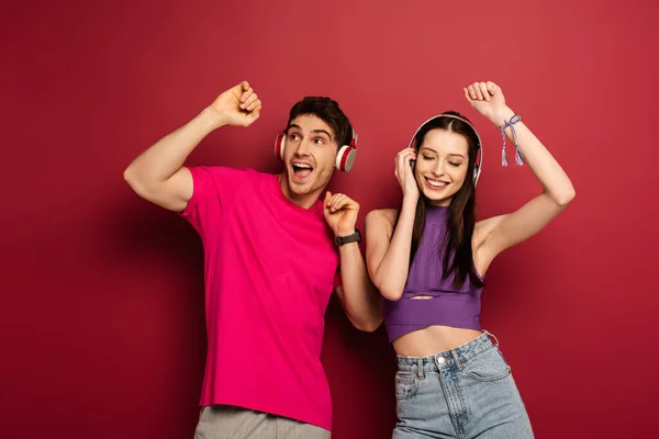 Beautiful couple dancing and listening music with headphones on red — Stock Photo