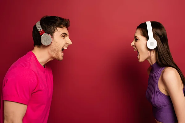 Aggressive couple in headphones yelling at each other on red — Stock Photo