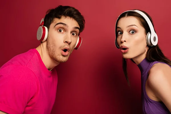 Beautiful surprised couple listening music with headphones on red — Stock Photo