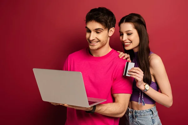 Beautiful happy couple shopping online with laptop and credit card on red — Stock Photo