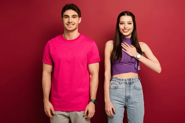 Handsome positive man and girlfriend with hand on heart on red — Stock Photo