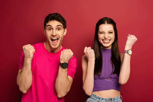 Excited emotional young couple holding fists on red — Stock Photo