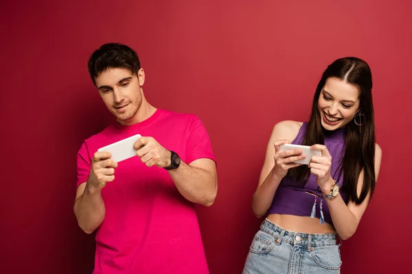 Beau couple émotionnel jouant sur les smartphones sur rouge — Photo de stock