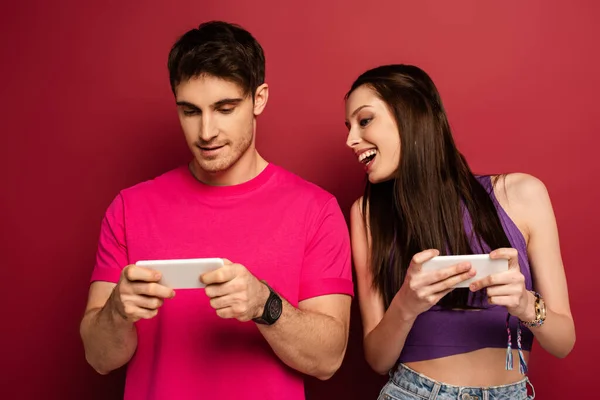 Beautiful happy couple playing on smartphones on red — Stock Photo