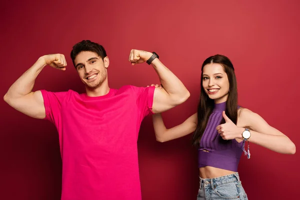 Strong musclar man with girlfriend showing thumb up on red — Stock Photo
