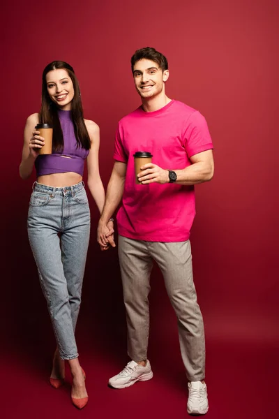 Beautiful couple with coffee to go holding hands on red — Stock Photo