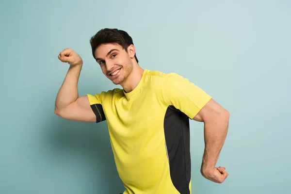 Muskulös lächelnder Sportler gestikuliert in gelbem T-Shirt auf blau — Stockfoto