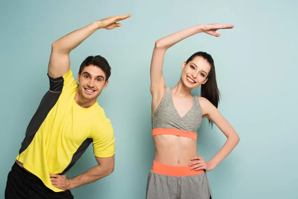 Happy athletic couple standing in sportswear exercising on blue — Stock Photo