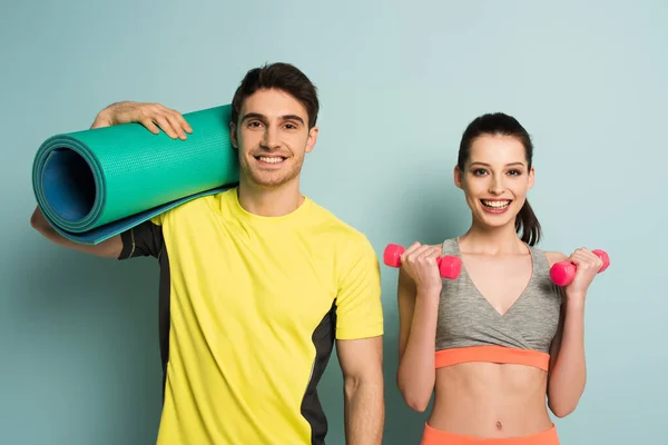 Happy athletic couple holding fitness mat and dumbbells on blue — Stock Photo