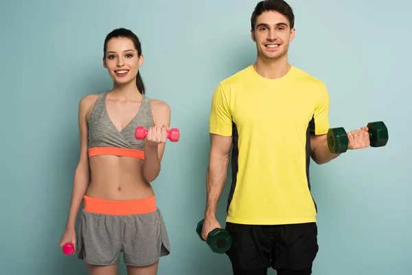 Cheerful athletic couple training with dumbbells on blue — Stock Photo