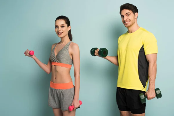 Cheerful athletic couple training with dumbbells on blue — Stock Photo
