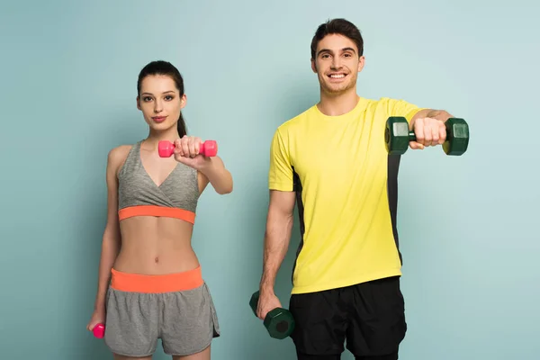 Beautiful happy athletic couple training with dumbbells on blue — Stock Photo