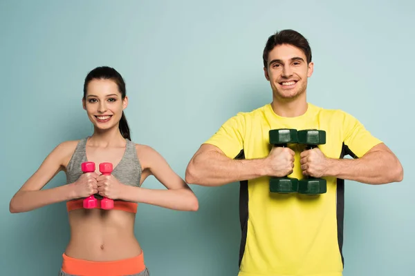Cheerful sportive couple holding dumbbells on blue — Stock Photo