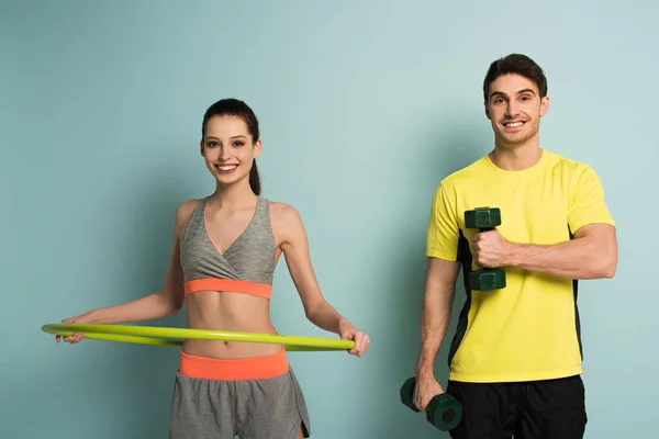 Cheerful athletic couple training with dumbbells and hula hoop on blue — Stock Photo