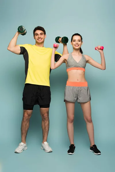 Sonriente pareja atlética sosteniendo mancuernas en azul - foto de stock