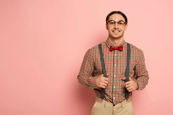 Улыбающийся мужчина-ботан в очках и подтяжках на розовом — стоковое фото