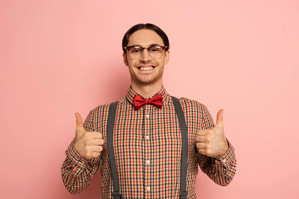 Alegre macho nerd en gafas mostrando pulgares hacia arriba en rosa - foto de stock