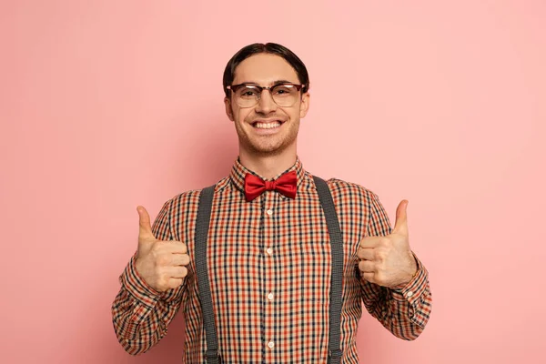 Alegre macho nerd en gafas mostrando pulgares hacia arriba en rosa — Stock Photo