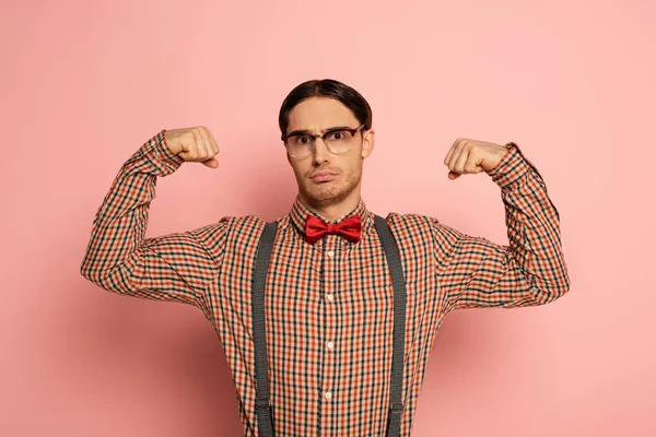 Nerd masculino emocional em óculos mostrando músculos em rosa — Fotografia de Stock