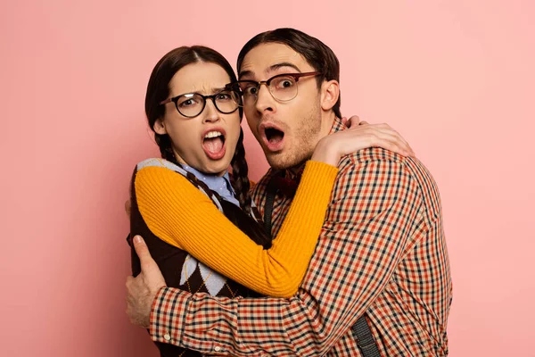 Couple of frightened nerds in eyeglasses hugging on pink — Stock Photo