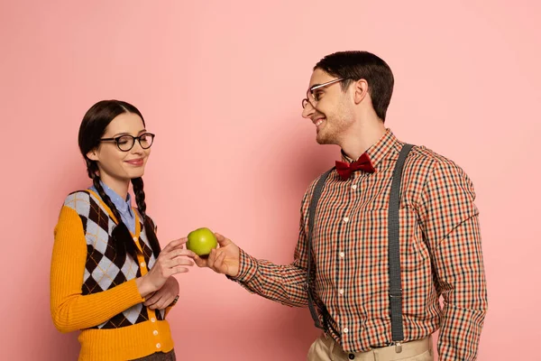 Couple of smiling nerds in eyeglasses holding apple on pink — Stock Photo