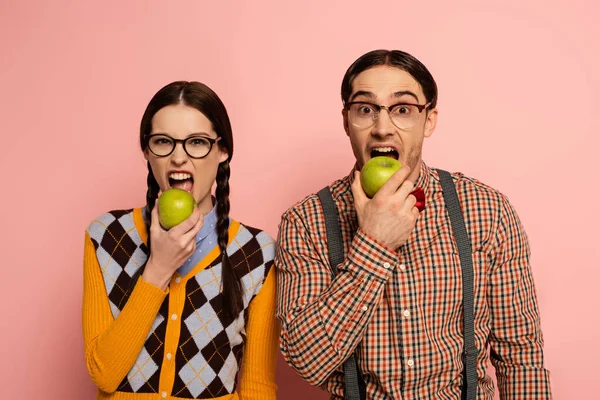 Couple of nerds in eyeglasses eating apples on pink — Stock Photo