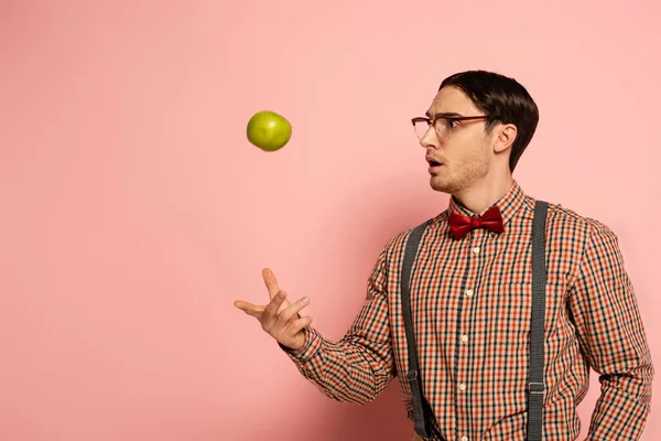 Shocked male nerd in eyeglasses throwing apple on pink — Stock Photo