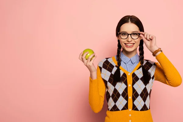 Smiling female nerd in eyeglasses holding apple on pink — Stock Photo