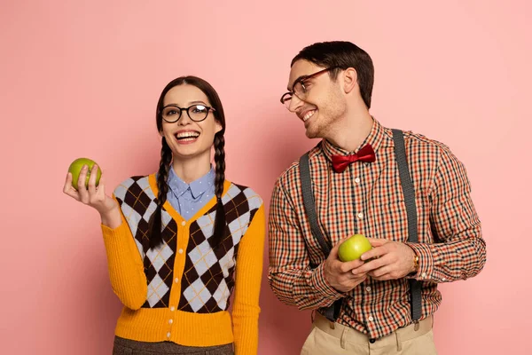 Couple of happy nerds in eyeglasses holding apples on pink — Stock Photo
