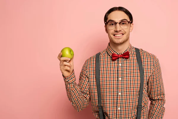 Cheerful male nerd in eyeglasses holding apple on pink — Stock Photo